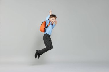 Sırt çantası açık gri arka planda atlayan sevimli okul çocuğu.