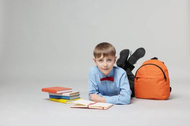 Sırt çantası açık gri arka planda kitap okuyan sevimli bir okul çocuğu.