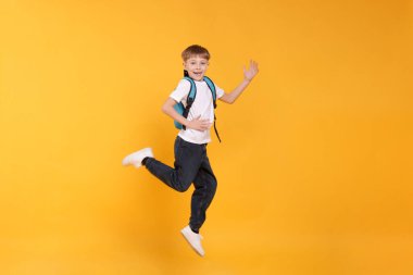 Turuncu arka planda atlayan sırt çantalı tatlı bir okul çocuğu.