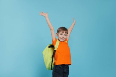 Açık mavi arka planda sırt çantası olan sevimli bir okul çocuğu.
