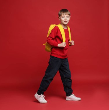 Kırmızı arka planda sırt çantası olan tatlı bir okul çocuğu.