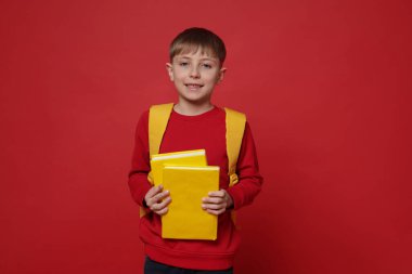 Sırt çantası ve kırmızı arka plan kitapları olan tatlı bir okul çocuğu.