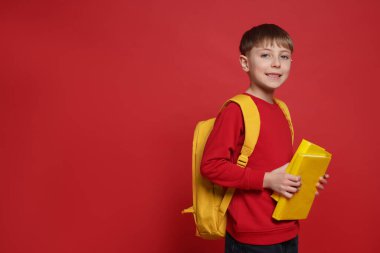 Sırt çantası ve kırmızı arkaplan kitapları olan sevimli bir okul çocuğu.