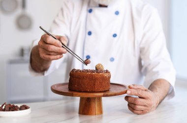 Yaşlı pasta şefi mutfaktaki masada lezzetli pastayı dekore ediyor, yakın plan.