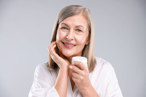 Улыбающаяся женщина с банкой коллагенового крема на сером фоне