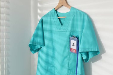 Beyaz duvara asılmış rozetli bir sağlık görevlisi üniforması.