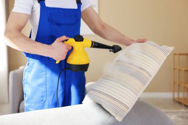 Temizlikçi yastığı evde buhar temizleyicisiyle temizliyor.