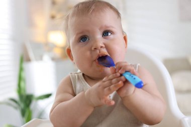 Evde kaşıkla yemek yiyen şirin bir bebek.