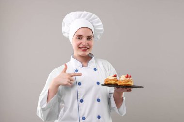 Üniformalı şekerci açık gri arka planda lezzetli profiteroller tutuyor.