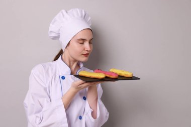 Üniformalı şekerlemeci açık gri arka planda lezzetli ekinler tutuyor, metin için yer var.