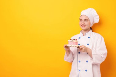 Üniformalı pastacı turuncu arka planda lezzetli bir pasta tutuyor, mesaj için yer var.