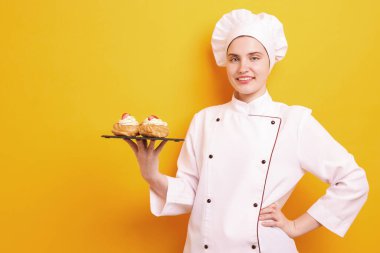 Üniformalı şekerlemeci turuncu arka planda lezzetli profiteroller tutuyor, mesaj için yer var.