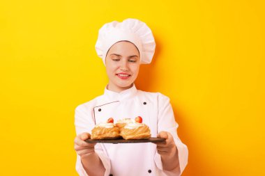 Üniformalı şekerci turuncu arka planda lezzetli profiteroller tutuyor.