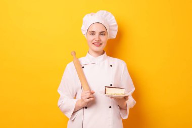 Üniformalı pastacı elinde oklavayla turuncu arka planda lezzetli bir pasta tutuyor.