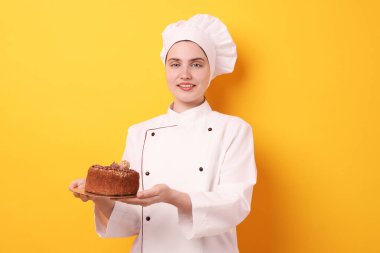 Üniformalı şekerlemeci turuncu arka planda lezzetli çikolatalı pasta tutuyor.