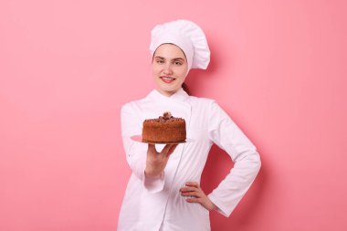 Üniformalı pastacı pembe arka planda lezzetli çikolatalı pasta tutuyor.