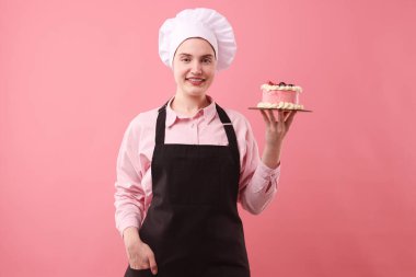 Şekerci pembe arka planda lezzetli bir pasta tutuyor.