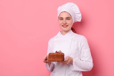 Üniformalı pastacı pembe arka planda çikolatalı kek tutuyor, mesaj için yer var.