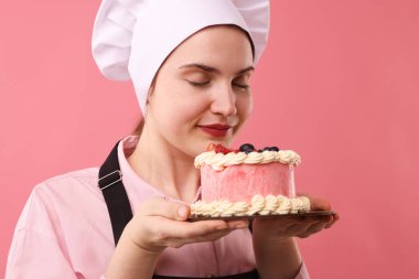 Şekerci pembe arka planda lezzetli bir pasta tutuyor.