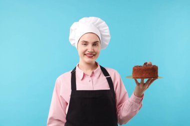 Açık mavi arka planda lezzetli çikolatalı pasta yapan bir pastacı.