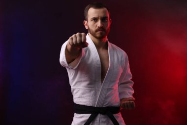 Üniformalı bir adam renkli ışıklarla ve dumanla karate yapıyor.