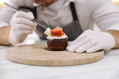 Mutfaktaki beyaz mermer masada çikolata traşlı lezzetli bir tatlıyı dekore eden şekerci, yakın plan.