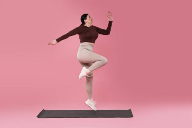 Ayrıca spor elbiseli kadın pembe arka planda egzersiz yapıyor.