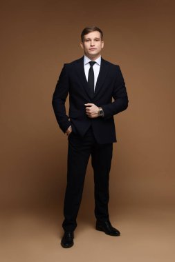 Kahverengi arka planda şık saati olan klasik takım elbiseli bir adam.