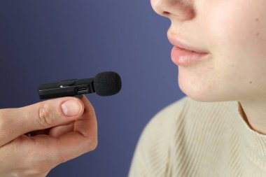 Açık mavi arka planda lavalier mikrofona konuşan kadın, yakın plan.