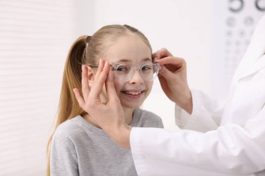 Vizyon testi. Oftalmolog klinikteki küçük kıza gözlük veriyor, yakın plan.
