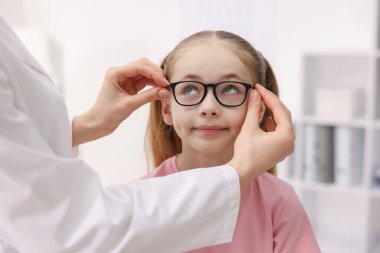 Vizyon testi. Oftalmolog klinikteki küçük kıza gözlük veriyor, yakın plan.