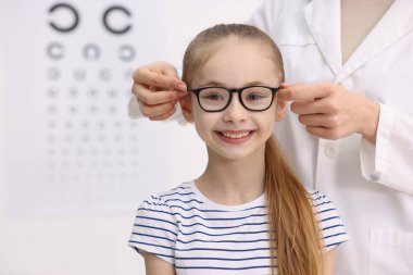 Vizyon testi. Oftalmolog klinikteki küçük kıza gözlük veriyor, yakın plan.