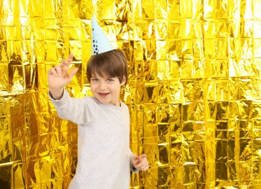Altın folyo perdenin yanında, kağıt şapkalı şirin çocuk, mesaj için yer var. Doğum günü sürpriz partisi
