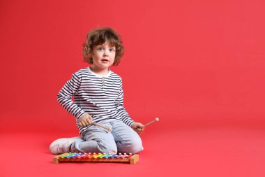 Kırmızı arka planda oyuncak ksilofon çalan şirin bir çocuk. Metin için boşluk