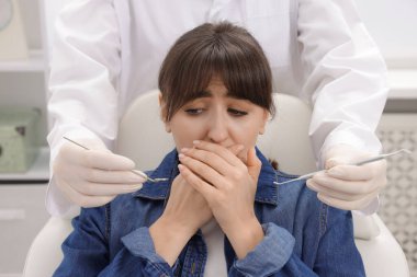 Klinikte ağzı ve dişçiyi aletlerle kaplayan korkmuş kadın.
