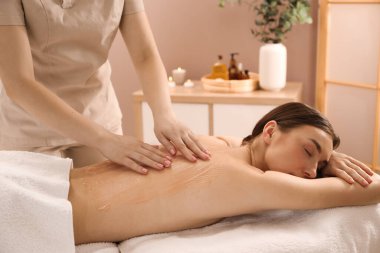 Vücut sargısı için kozmetik ürünler uygulayan estetikçi kaplıca salonundaki kadının sırtına sarıp kapatıyor.