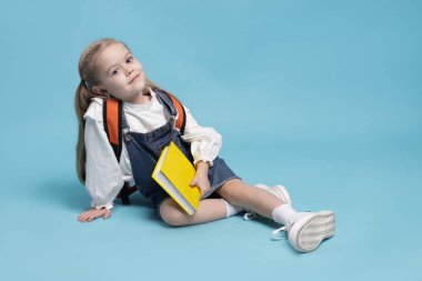 Sırt çantası ve açık mavi arka plan kitabı olan tatlı bir kız öğrenci. Metin için boşluk