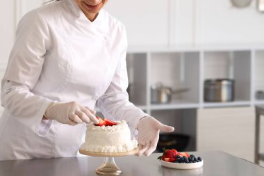 Pastacı mutfakta çilekle pasta süslüyor.