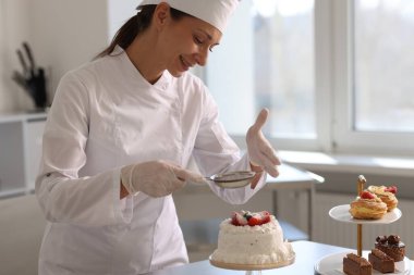 Şekerci, mutfaktaki kekin üzerine pudra şekeri serpiyor.