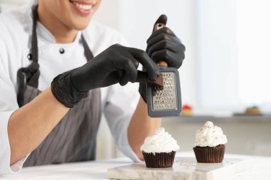 Şekerci çikolatayı mutfaktaki masada kekin üzerine rendeliyor.