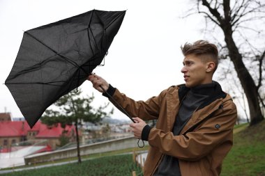 Kırık şemsiyeli bir adam açık havada yağmur altında rüzgarla savaşıyor.