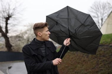 Kırık şemsiyeli bir adam açık havada yağmur altında rüzgarla savaşıyor.