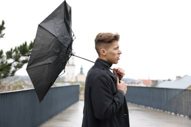 Kırık şemsiyeli bir adam açık havada yağmur altında rüzgarla savaşıyor.