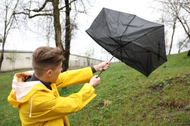 Kırık şemsiyeli bir adam açık havada yağmur altında rüzgarla savaşıyor.