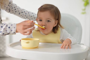 Annesi küçük bebeğini yüksek sandalyede besliyor, yakın plan.