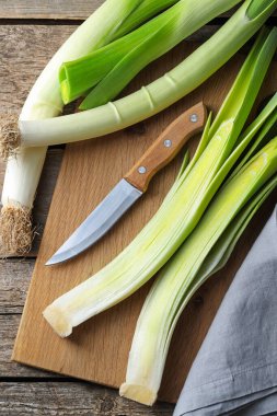 Whole fresh leeks, knife and towel on wooden table, top view