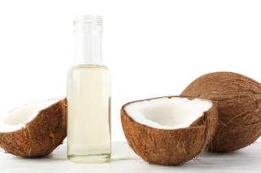Organic coconut cooking oil in glass bottle and fresh fruits on wooden table against white background