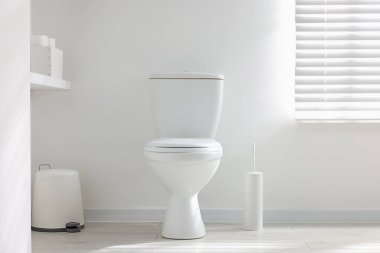 Tuvalet, fırça ve ihtiyaçlar banyoda beyaz duvarın yanında.