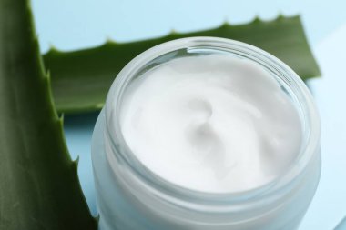 Açık mavi arkaplanda krema ve aloe yaprakları, yakın plan