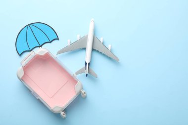 Seyahat sigortası. Uçak modeli, kağıt şemsiye ve açık mavi arka planda bavul, düz. Metin için boşluk